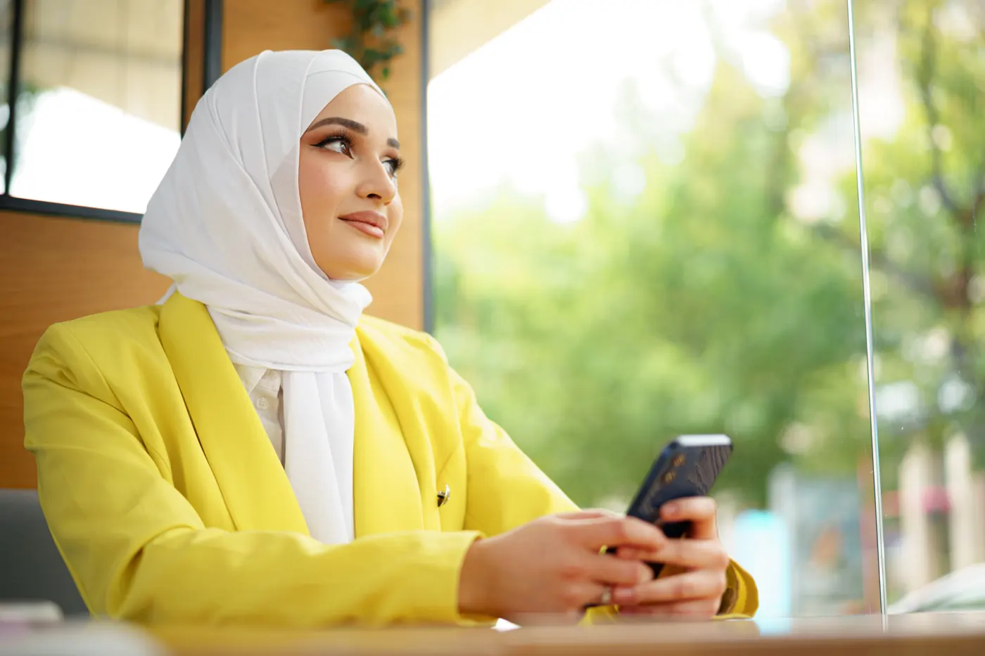 A woman in a hijab smiling at her phone in a bright café